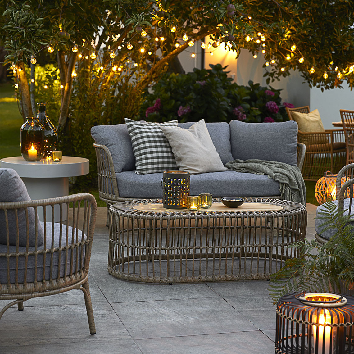 ILLERUP loungesæt, FINK lyskæde og SANDSVALE solcellelampe Lanterner, batterilamper og lyskæder lyser i aftemørket på en terrasse